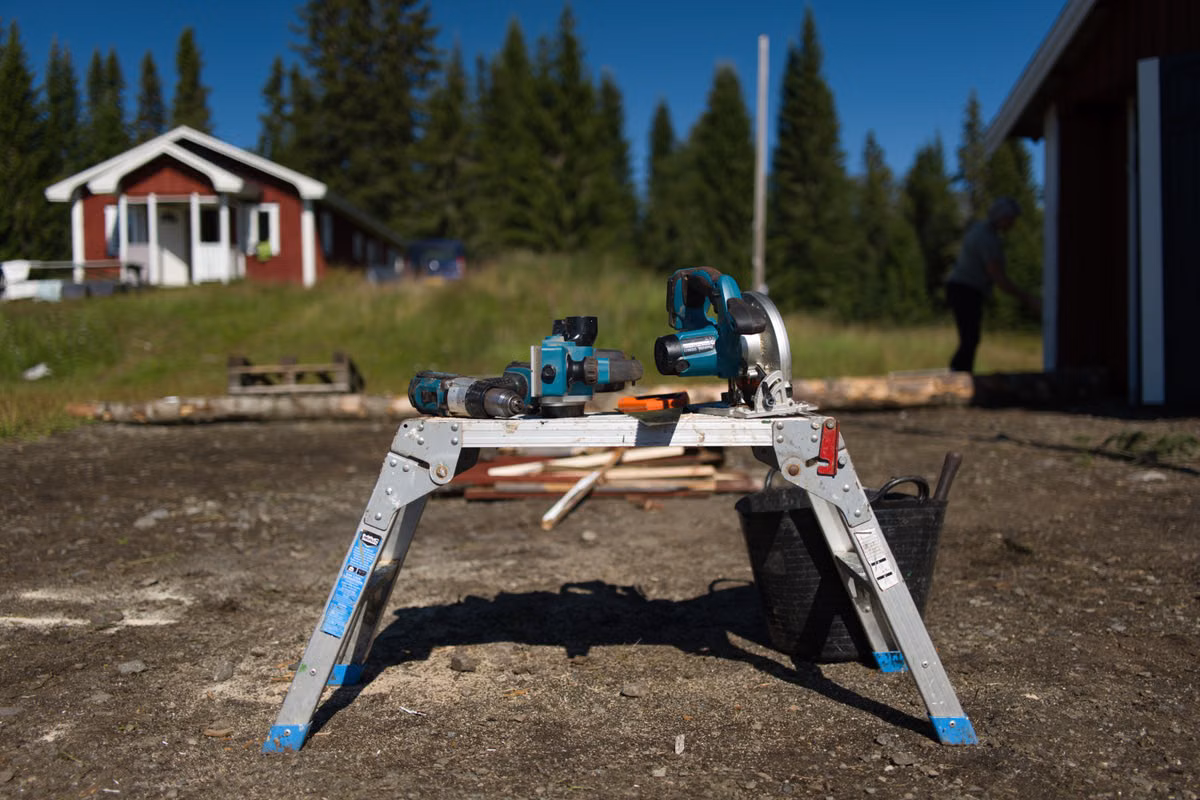 Cordless power tools, including a drill and a circular saw, left on a metal work platform on an outdoor building site.